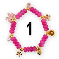 A pink beaded bracelet with gold-colored charms, including a bow, flowers, a heart, and a pearl. The bracelet has the number 1 in black in the center.