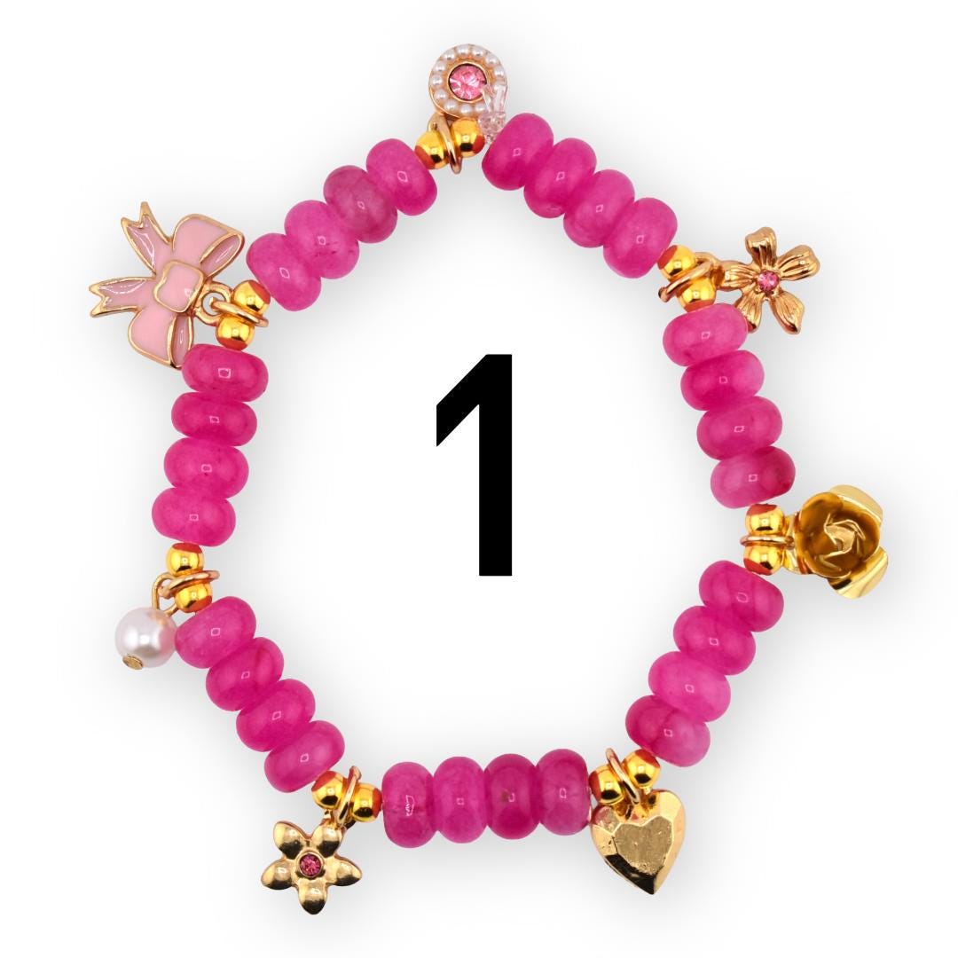 A pink beaded bracelet with gold-colored charms, including a bow, flowers, a heart, and a pearl. The bracelet has the number 1 in black in the center.