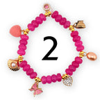 A magenta beaded bracelet with gold accents and various charms, including a heart, butterfly, seashell, and a small teapot. The bracelet also features a pink heart-shaped charm and a pearl-shaped charm. The number "2" is in the center.