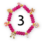 A magenta beaded bracelet with gold-colored charms. The charms include a heart, a flower, a bow, and a pearl. The number "3" is in the center of the bracelet.