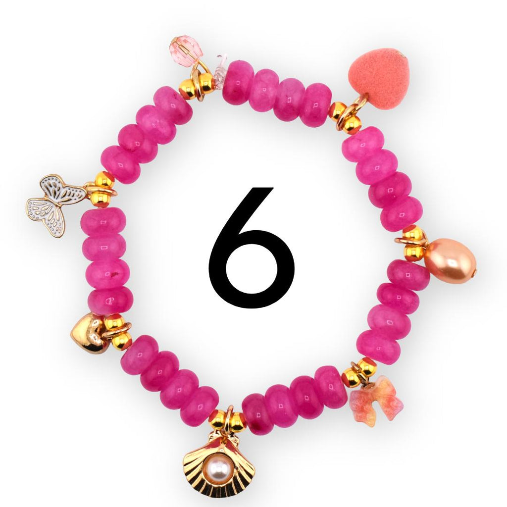 A pink beaded bracelet with gold accents and decorative charms. Charms include a butterfly, a seashell with a pearl, a heart, and a bow. The number 6 is in the center of the bracelet.