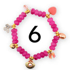 A pink beaded bracelet with gold accents and decorative charms. Charms include a butterfly, a seashell with a pearl, a heart, and a bow. The number 6 is in the center of the bracelet.