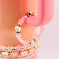 A collection of pink and clear beaded bracelets with silver accents. The bracelets feature various bead sizes and shapes, including round, faceted, and disc-shaped beads. The bracelets are displayed on a pink mug handle.