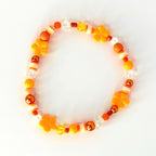 A beaded bracelet featuring a variety of orange beads, including flower-shaped beads, round beads, and cylindrical beads. The bracelet also includes clear and white beads, creating a colorful and playful accessory.