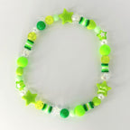 A beaded bracelet featuring a variety of green beads, including round, star-shaped, and cylindrical beads. The bracelet incorporates shades of lime, neon, and forest green, with clear and white accents. The bracelet is designed with a playful and youthful aesthetic.