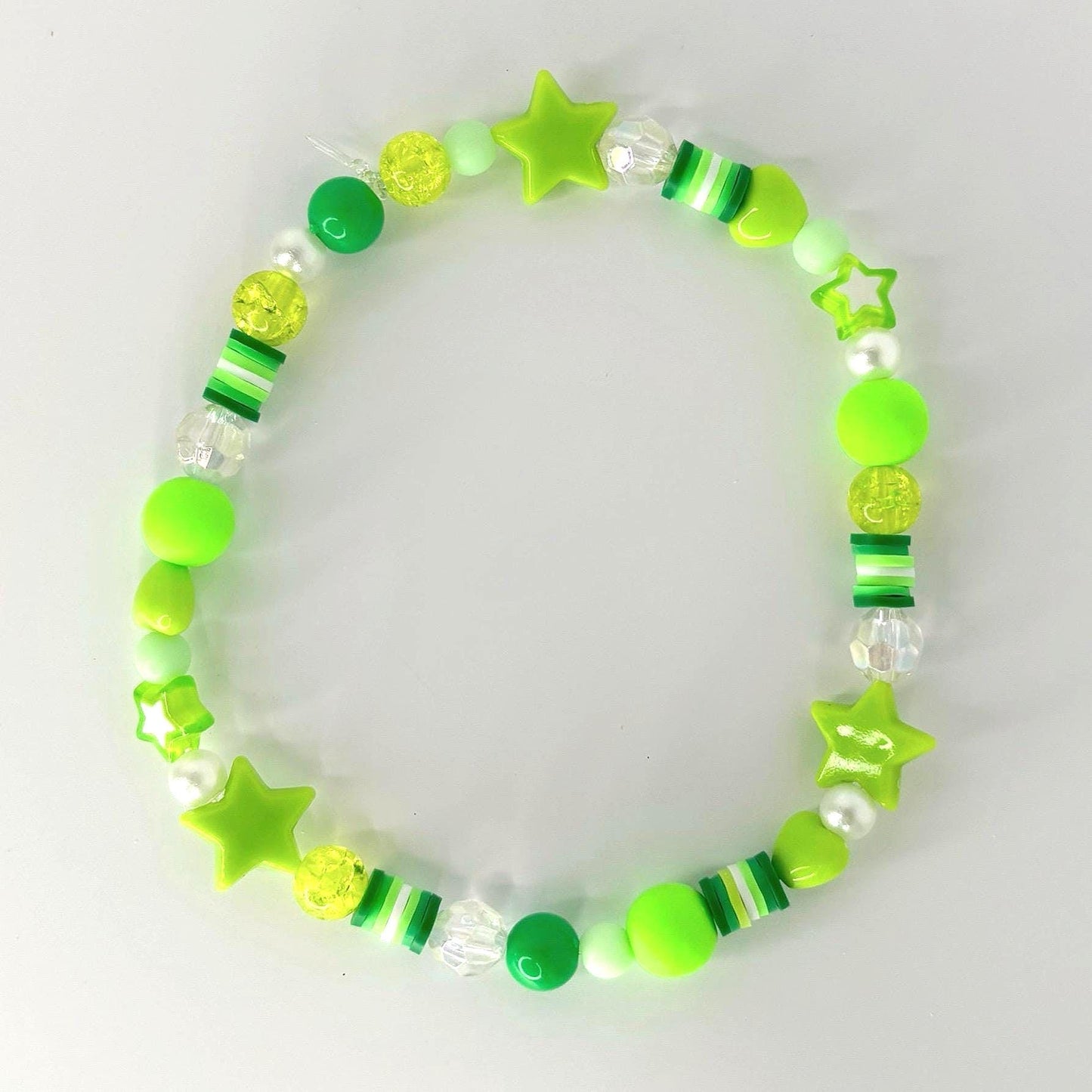 A beaded bracelet featuring a variety of green beads, including round, star-shaped, and cylindrical beads. The bracelet incorporates shades of lime, neon, and forest green, with clear and white accents. The bracelet is designed with a playful and youthful aesthetic.