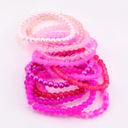 A collection of pink beaded bracelets in various shades, including light pink, hot pink, and fuchsia. The bracelets are made of different materials, including pearls and clear beads. The bracelets are stacked together on a white background.