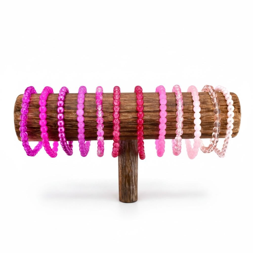 A wooden bracelet display stand holding a collection of beaded bracelets in shades of pink and purple. The bracelets are arranged in a gradient of colors, from deep magenta to pale pink. The stand is made of dark wood.