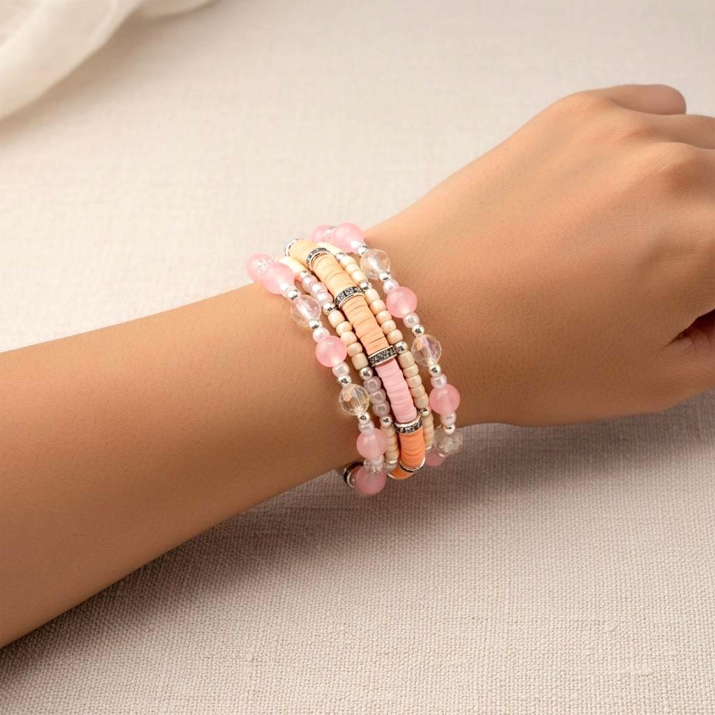 A multi-strand bracelet featuring a mix of beads in shades of pink, peach, and clear. The bracelet includes round and disc-shaped beads, with silver-toned accents. The bracelet is wrapped around a wrist.
