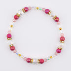 A beaded bracelet featuring alternating fuchsia and clear beads. The bracelet includes gold-colored spacers and accents. The beads are strung on a clear elastic cord, creating a delicate and elegant accessory.