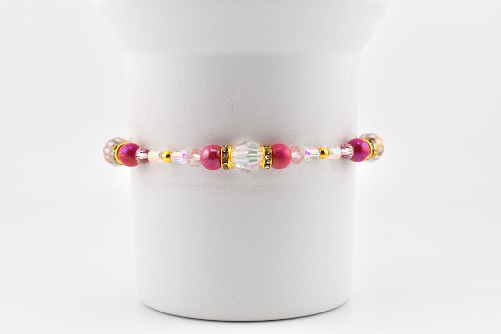 A beaded bracelet featuring a combination of pink, gold, and clear beads. The bracelet has a central section with a large clear bead and smaller pink beads, with gold accents and smaller pink and clear beads on either side.