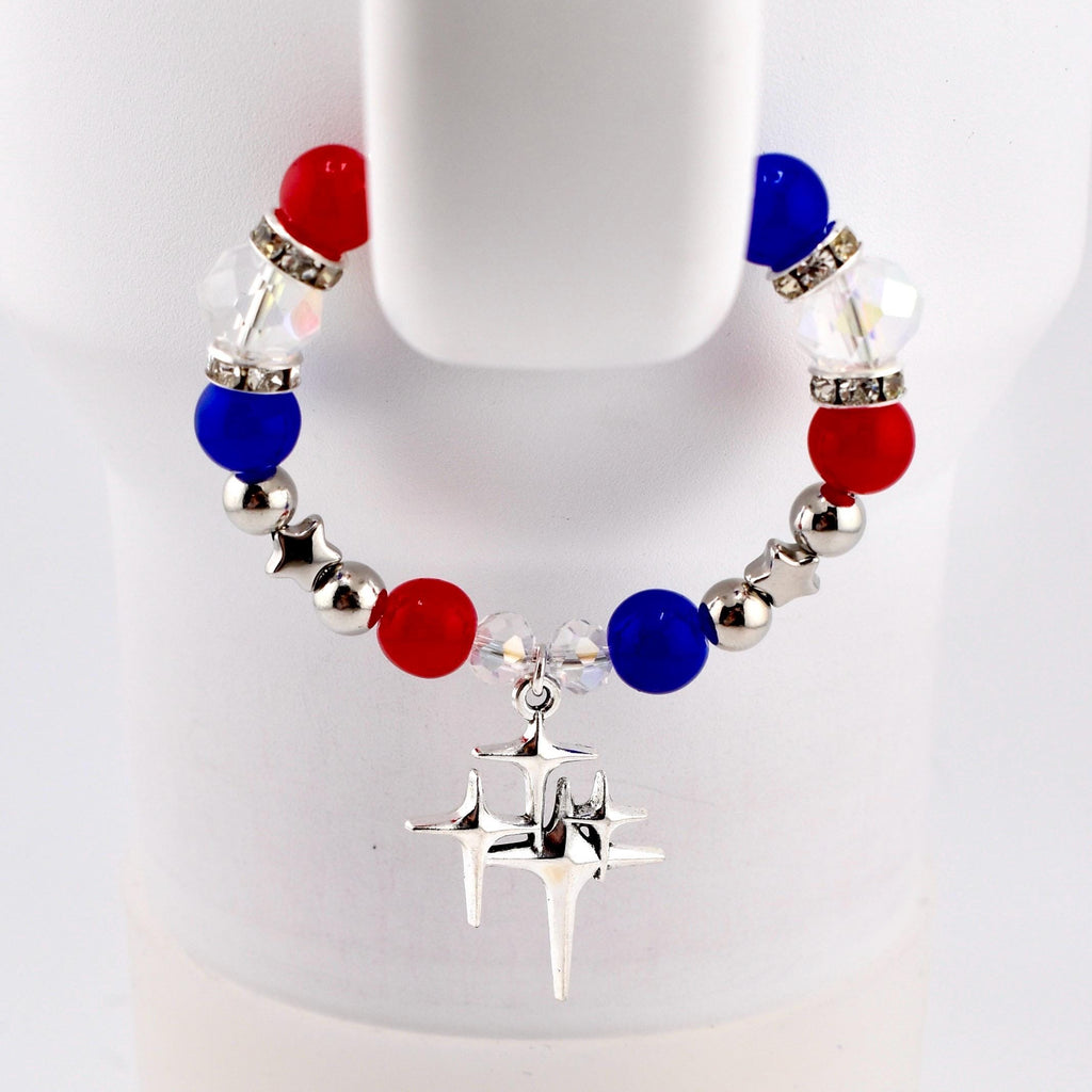 A patriotic bracelet featuring red, white, and blue beads, interspersed with silver star-shaped beads. The bracelet has a silver charm with a starburst design.