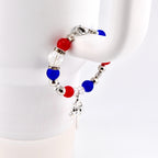 A patriotic bracelet featuring red, white, and blue beads, interspersed with silver-colored beads. A small silver charm hangs from the bracelet. The bracelet is secured with a silver clasp.