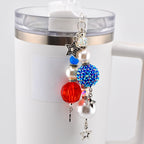A patriotic-themed charm with red, white, and blue beads and star accents. The charm is attached to a white tumbler. The charm features a faceted red bead, a blue rhinestone-covered bead, and a pearl bead.