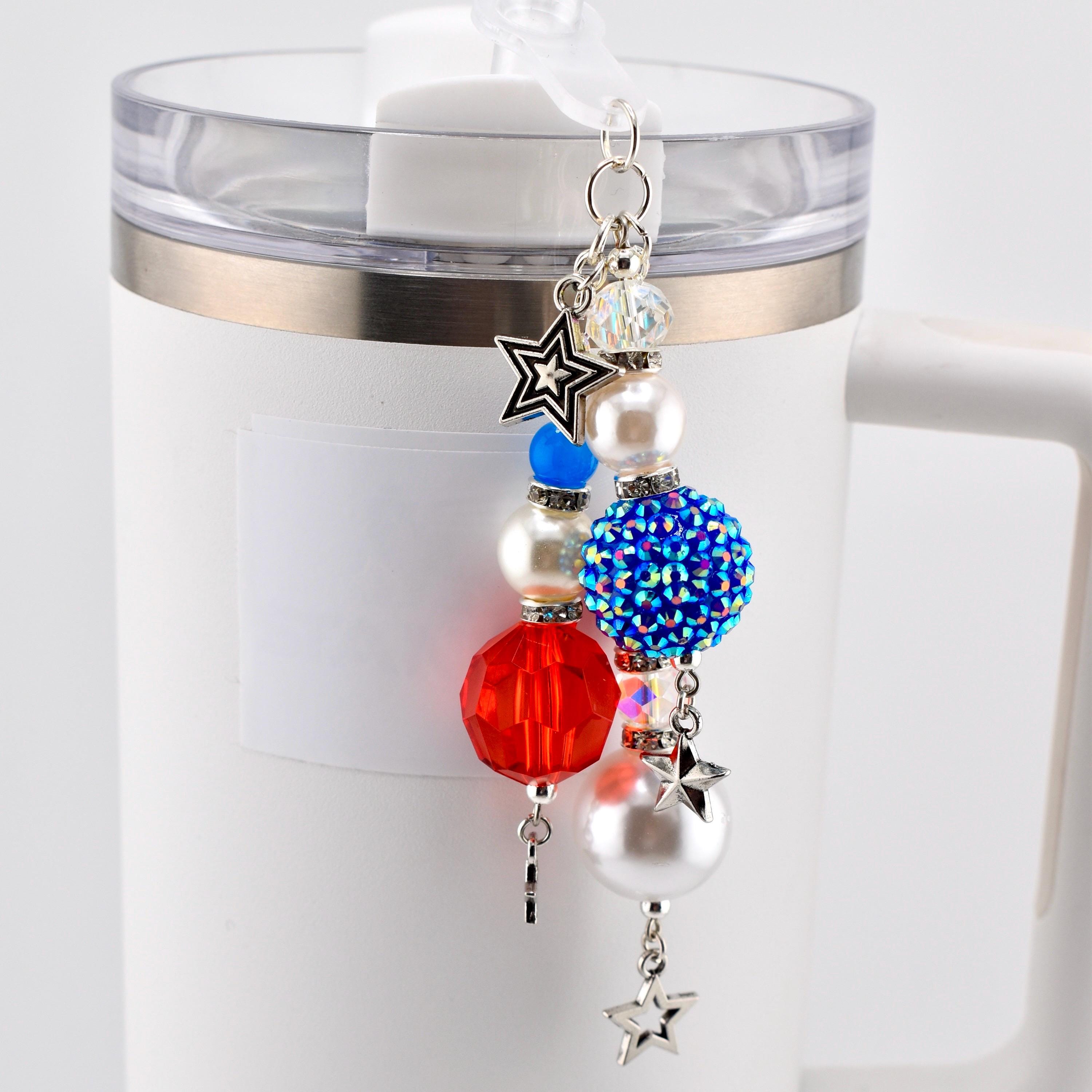 A patriotic-themed charm with red, white, and blue beads and star accents. The charm is attached to a white tumbler. The charm features a faceted red bead, a blue rhinestone-covered bead, and a pearl bead.