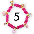A pink beaded bracelet with gold accents and charms. Charms include a teacup, bow, heart, and a pink leaf. The number 5 is in the center of the bracelet.