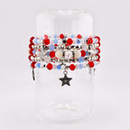 A collection of beaded bracelets in red, white, and blue, with silver accents and star charms. The bracelets are displayed on a clear glass cylinder, showcasing the patriotic color scheme and intricate beadwork. The bracelets feature a variety of bead sizes and textures.