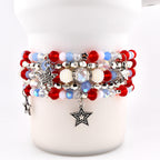 A stack of beaded bracelets in red, white, and blue. The bracelets feature various bead sizes and textures, including round red beads, clear beads, and white pearl-like beads. Silver star charms dangle from the bracelets.