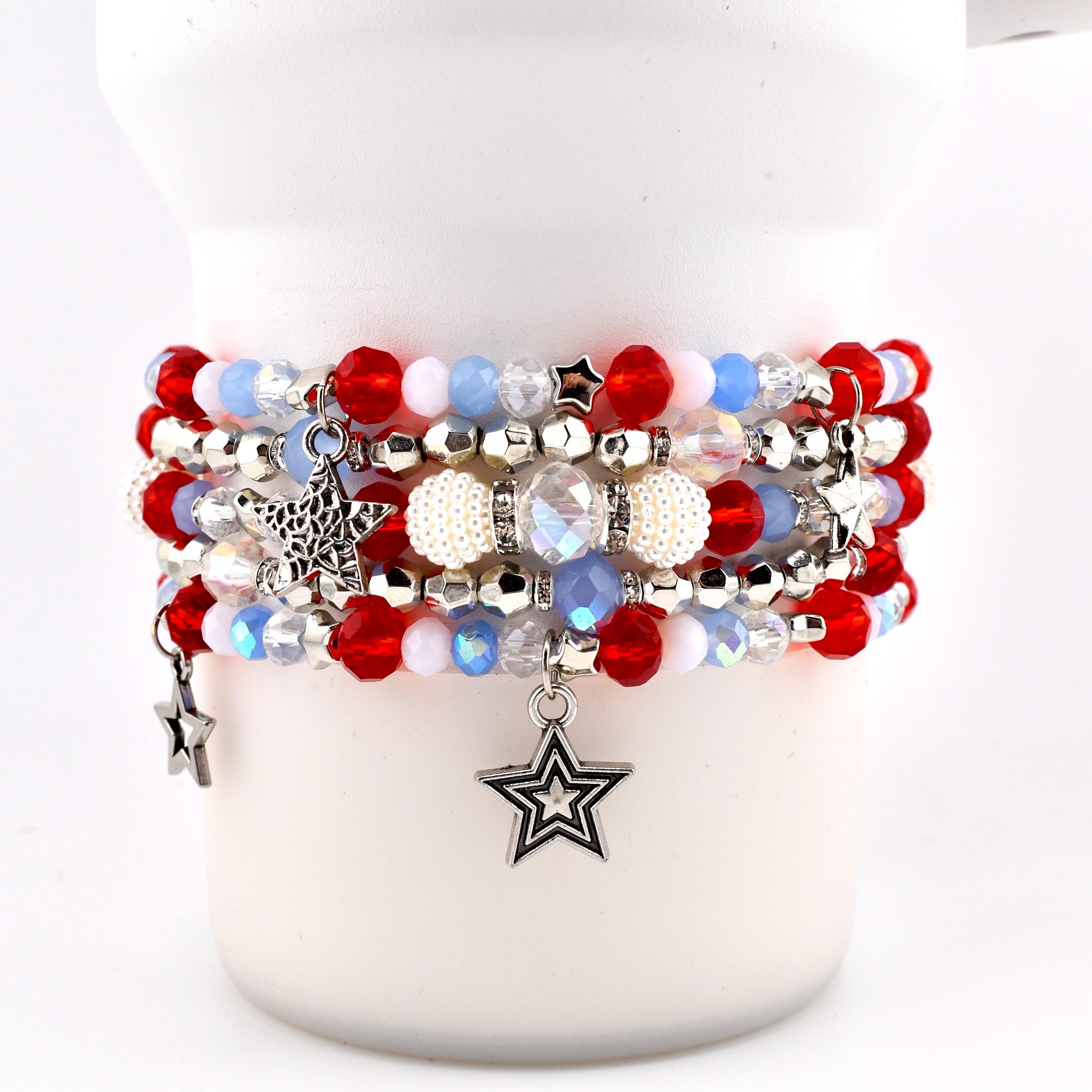 A stack of beaded bracelets in red, white, and blue. The bracelets feature various bead sizes and textures, including round red beads, clear beads, and white pearl-like beads. Silver star charms dangle from the bracelets.