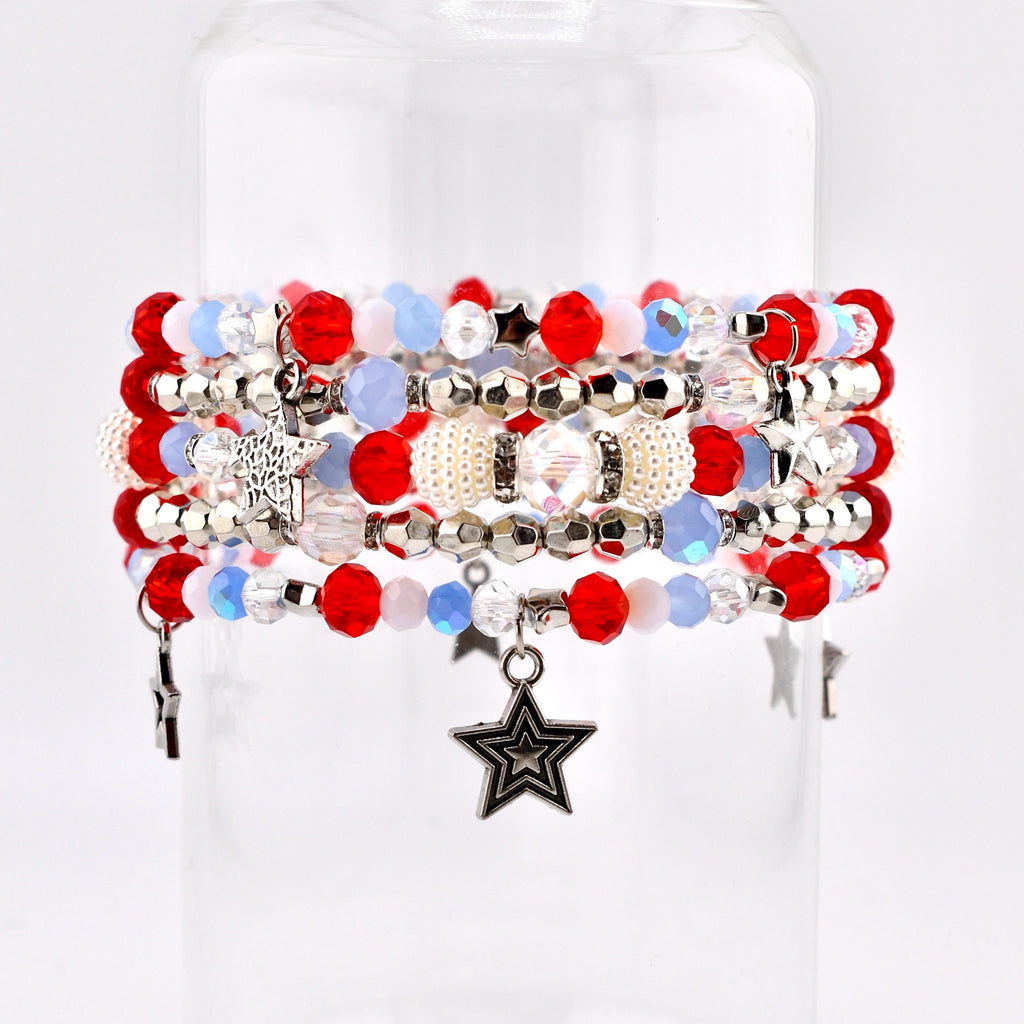 A stack of beaded bracelets in red, white, and blue. The bracelets feature various bead sizes and shapes, including round, faceted, and pearl-like beads. Some bracelets have star-shaped charms.