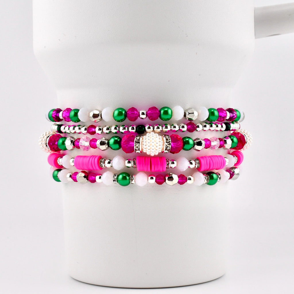 A stack of five beaded bracelets in shades of pink, green, white, and silver. The bracelets feature various bead sizes and textures, including small round beads, larger faceted beads, and flat disc beads. The bracelets are displayed on a white background.
