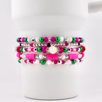 A stack of five beaded bracelets in shades of pink, green, white, and silver. The bracelets feature various bead sizes and textures, including small round beads, larger faceted beads, and flat disc beads. The bracelets are displayed on a white background.