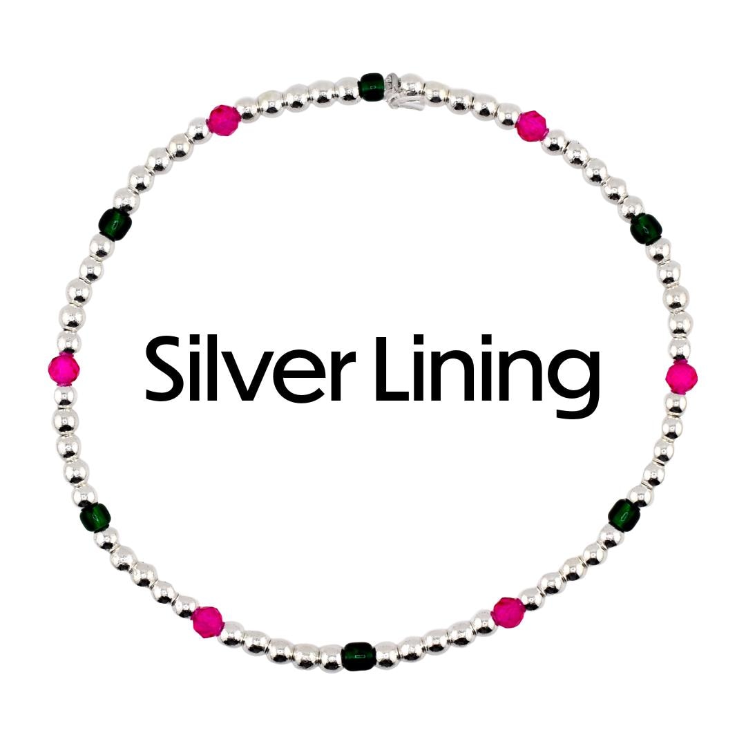 A silver beaded bracelet with alternating pink and green beads. The bracelet is circular and features the text "Silver Lining" in black. The beads are small and evenly spaced.