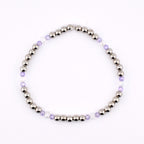 A silver beaded bracelet with alternating sections of silver beads, clear beads, and light purple beads. The bracelet is strung together and is displayed on a white background. The bracelet is a piece of jewelry.