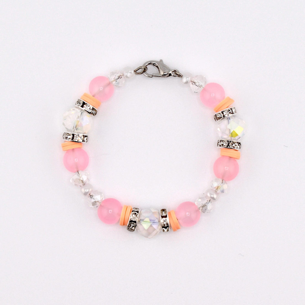 A delicate bracelet featuring pink and clear beads, accented with silver-toned spacers and orange-colored cylindrical beads. The bracelet is secured with a silver clasp. The beads are strung together, creating a circular design.