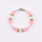 A delicate bracelet featuring pink and clear beads, accented with silver-toned spacers and orange-colored cylindrical beads. The bracelet is secured with a silver clasp. The beads are strung together, creating a circular design.