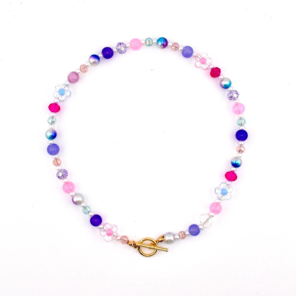 A colorful beaded necklace featuring a variety of beads in shades of pink, purple, blue, and clear. The necklace includes flower-shaped beads and a gold-colored toggle clasp. The beads are strung together to create a circular design.