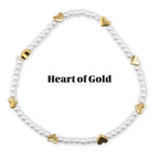 A white beaded bracelet with gold heart-shaped charms. The bracelet is circular and features the text "Heart of Gold" in the center. The bracelet is on a white background.