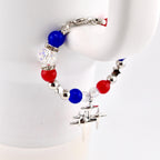A patriotic Stanley tumbler handle bracelet featuring red, white, and blue beads, interspersed with silver star-shaped accents and a dangling silver charm. The bracelet is held against a white background, showcasing its vibrant colors and design.
