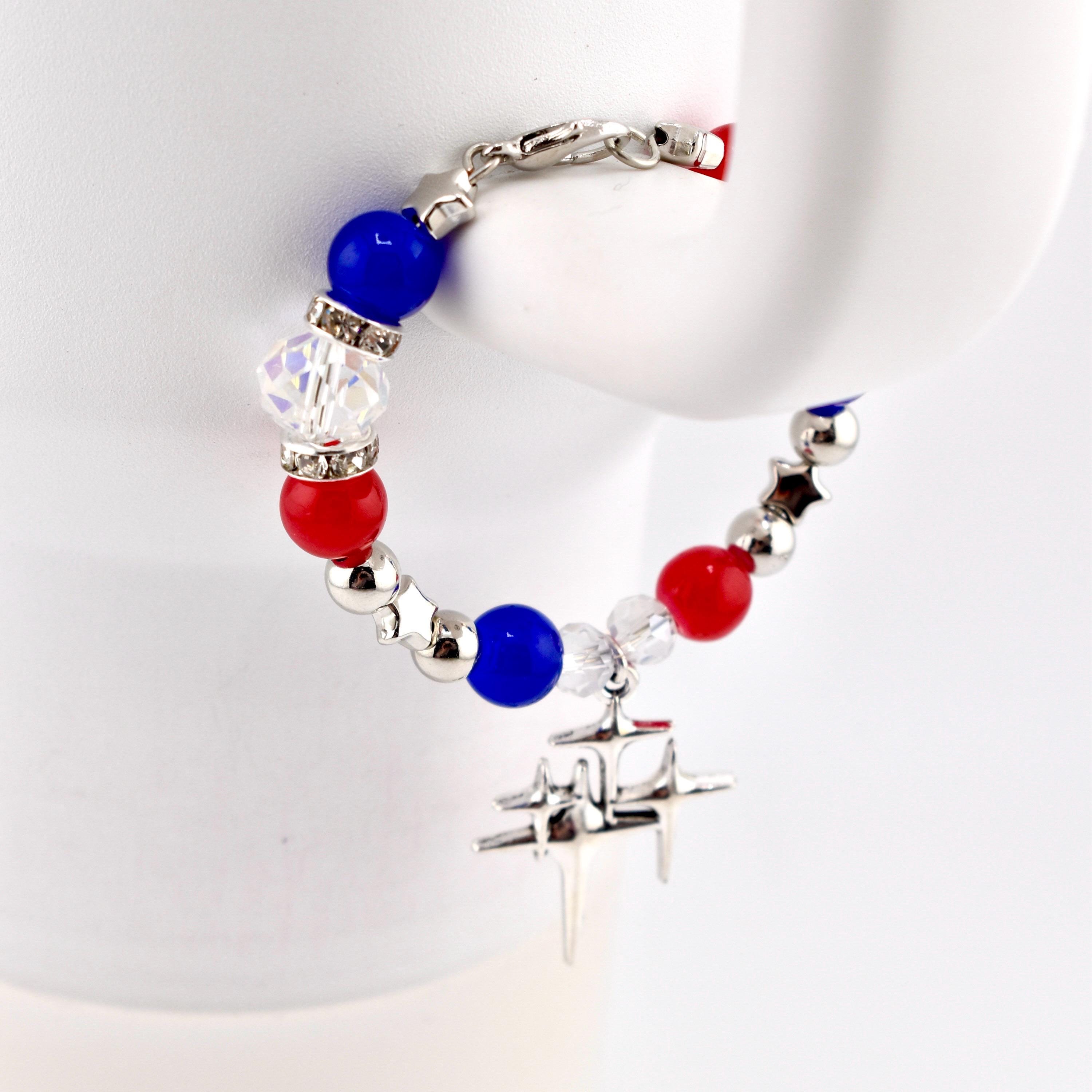 A patriotic Stanley tumbler handle bracelet featuring red, white, and blue beads, interspersed with silver star-shaped accents and a dangling silver charm. The bracelet is held against a white background, showcasing its vibrant colors and design.