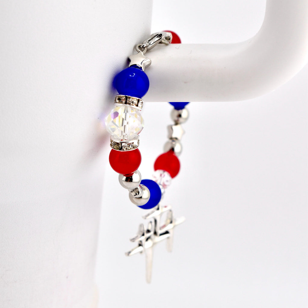 A patriotic bracelet featuring red, white, and blue beads. The bracelet includes round red and blue beads, clear crystal beads, and silver-toned star-shaped accents. A silver charm hangs from the bracelet.