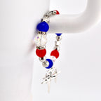 A patriotic bracelet featuring red, white, and blue beads. The bracelet includes round red and blue beads, clear crystal beads, and silver-toned star-shaped accents. A silver charm hangs from the bracelet.