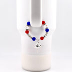 A red, white, and blue beaded tumbler charm bracelet with a silver-colored starburst charm. The handle bracelet is attached to a white mug. The beads are round and interspersed with silver-colored beads and clear crystal beads.