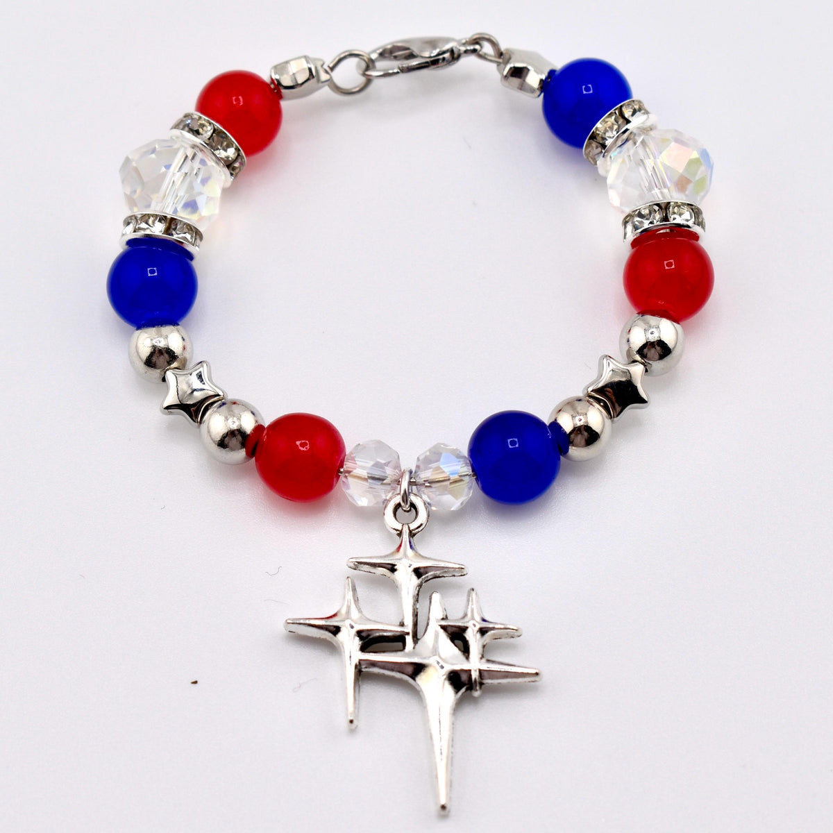 A patriotic bracelet featuring red, white, and blue beads, interspersed with silver accents. The bracelet includes a charm with a starburst design. The beads are round and faceted, creating a sparkling effect. The bracelet is secured with a silver clasp.