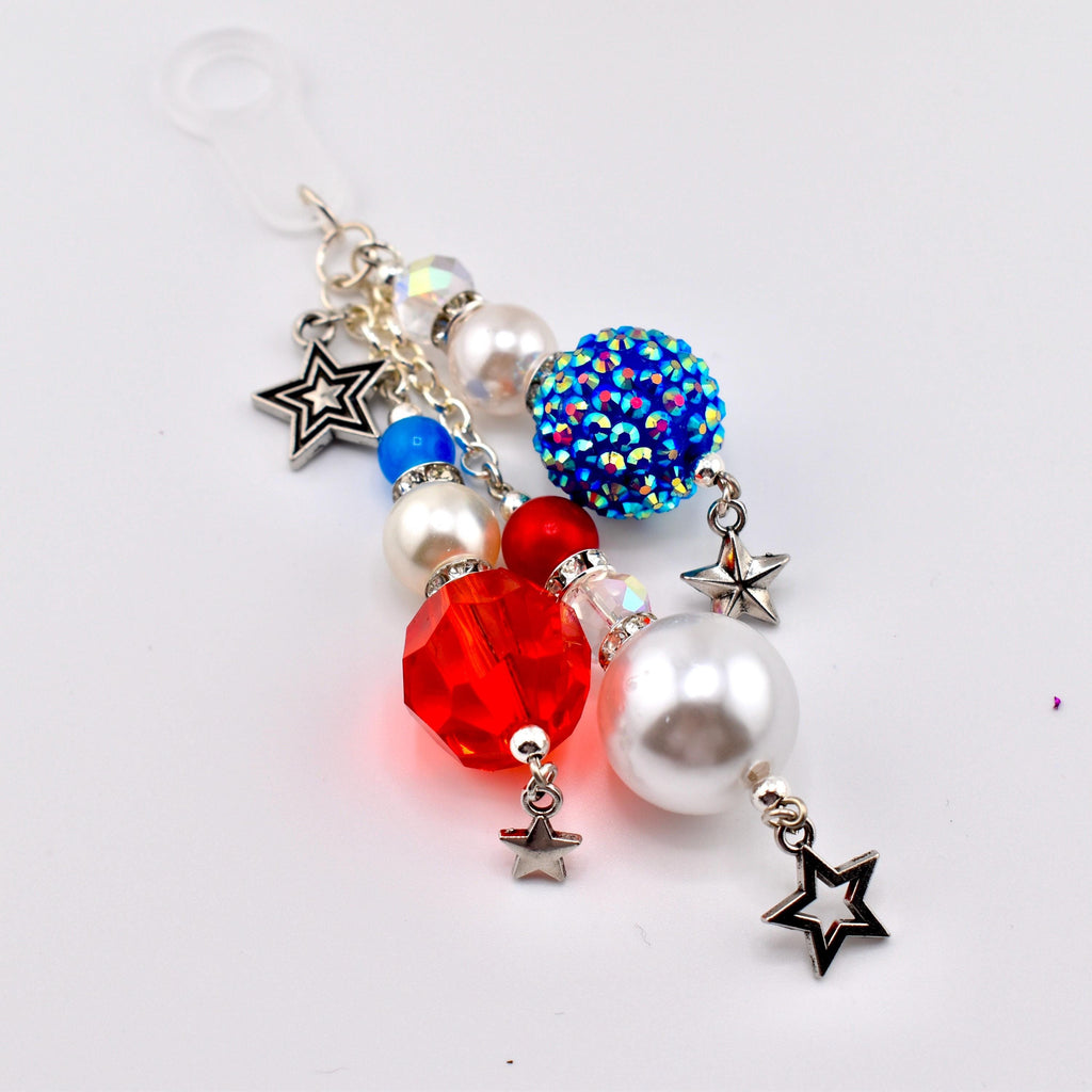 A patriotic-themed charm featuring a variety of beads in red, white, and blue. The charm includes a large red faceted bead, a blue rhinestone-covered bead, and several white pearl beads. Silver star charms dangle from the beads.