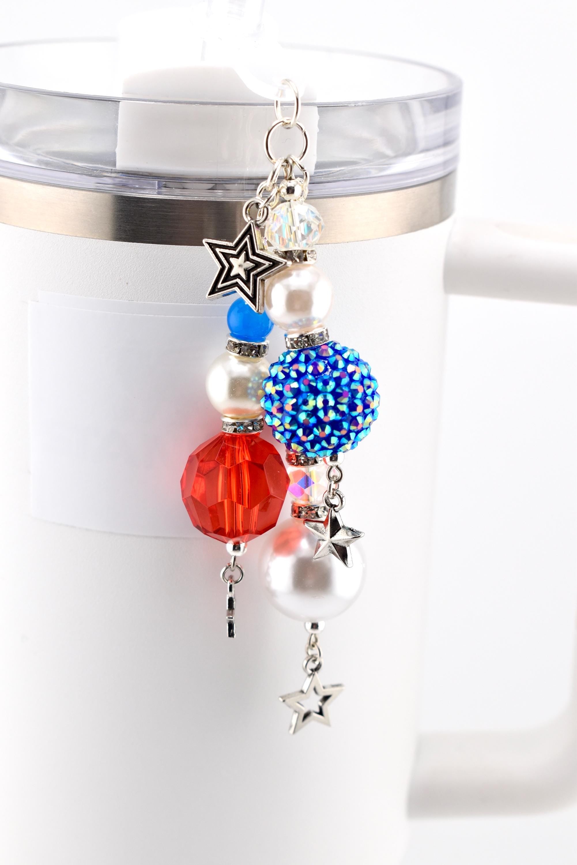 A patriotic-themed charm with red, white, and blue beads and star accents. The charm features a faceted red bead, a blue rhinestone-covered bead, and several pearl-like beads. Silver-toned star charms dangle from the bottom.