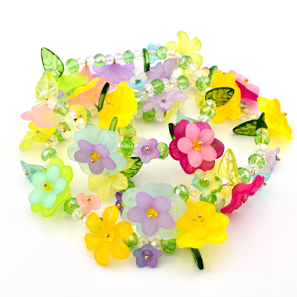 A colorful floral necklace featuring translucent flowers in shades of yellow, pink, purple, and blue. The flowers are strung together with clear beads and green leaves, creating a vibrant and whimsical accessory.
