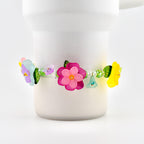 A floral bracelet with colorful flower beads. The bracelet features a large pink flower in the center, with smaller purple, blue, and yellow flowers. The bracelet is adorned with green leaves and clear beads.