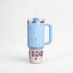 A light blue insulated tumbler with a handle, lid, and straw. The tumbler is decorated with red, white, and blue stars. A beaded bracelet with red, white, and silver beads and a star charm is wrapped around the base.