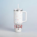 White insulated tumbler with a handle, lid, and straw. The tumbler is decorated with red, white, and blue stars. A band of red, white, and blue beads and star charms adorns the bottom of the tumbler.