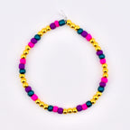 A colorful beaded bracelet featuring gold, magenta, teal, and purple beads. The bracelet is strung on a clear elastic cord. This handmade jewelry piece is suitable for everyday wear.