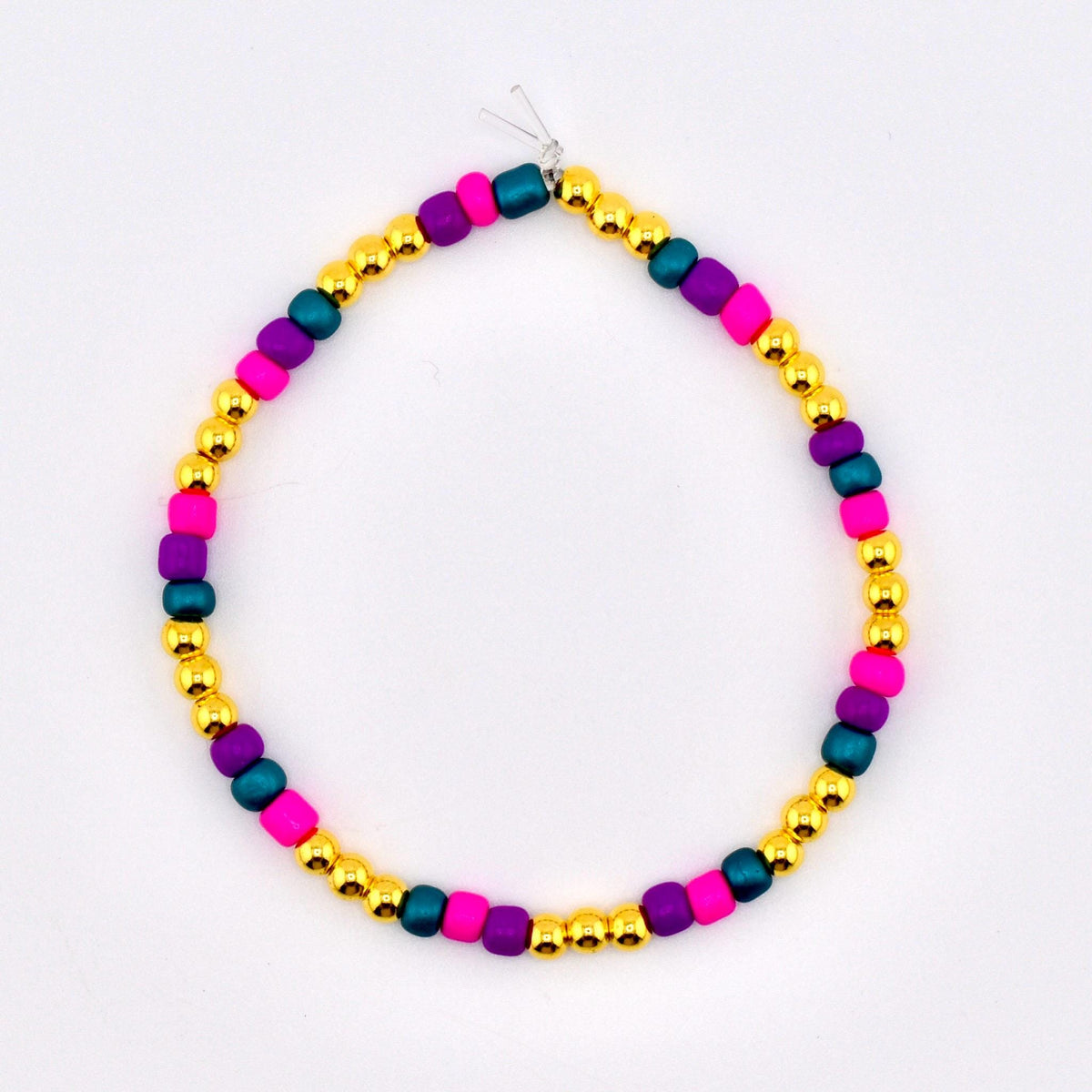A colorful beaded bracelet featuring gold, magenta, teal, and purple beads. The bracelet is strung on a clear elastic cord. This handmade jewelry piece is suitable for everyday wear.