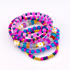 A stack of colorful beaded bracelets. The bracelets feature a variety of beads in shades of pink, blue, purple, and gold. Some bracelets have white daisy-shaped beads.