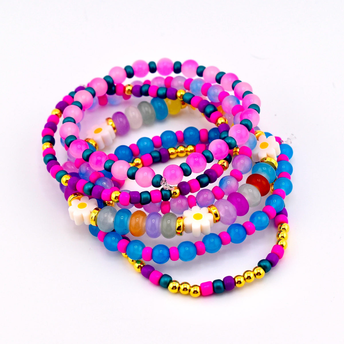 A stack of colorful beaded bracelets. The bracelets feature a variety of beads in shades of pink, blue, purple, and gold. Some bracelets have white daisy-shaped beads.