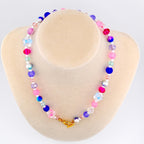 A colorful beaded necklace with a gold clasp. The necklace features a variety of beads in shades of pink, blue, purple, and white. Some beads are flower-shaped. The necklace is displayed on a mannequin.