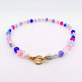 A colorful beaded necklace featuring a variety of beads in shades of pink, purple, blue, and clear. The necklace includes flower-shaped beads and a gold-colored toggle clasp. The beads are strung together to create a delicate and eye-catching accessory.